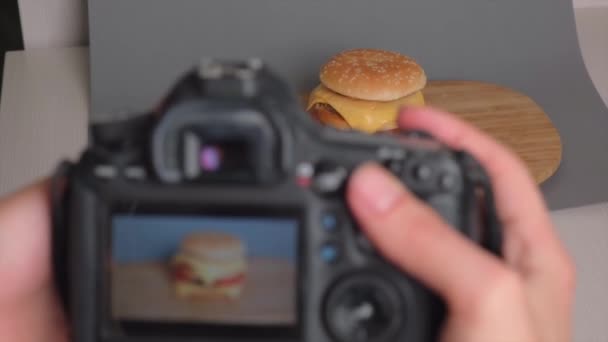 Uma mão segura uma câmera e atira em um grande hambúrguer duplo suculento. Fast food. — Vídeo de Stock