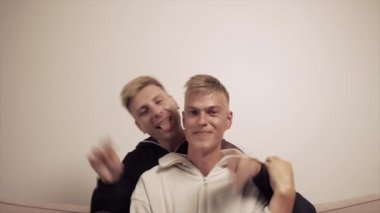 Adam bir barış jesti gösteriyor. İki adam kameraya bakıyor..