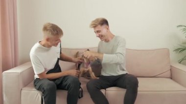 Kanepede bir köpekle otururken evde oynayan eşcinsel çift..