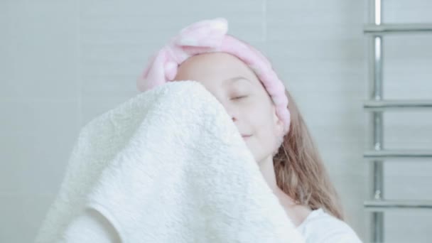 A beautiful cute girl wipes her face with a white towel, looks into the camera. — Stock Video