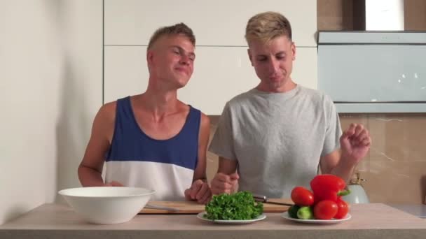 Dos precioso gay chicos en un brillante cocina están preparando desayuno ensalada. — Vídeo de stock