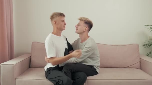 Gay paar chatten terwijl zitten op de bank knuffelen en lachen. — Stockvideo