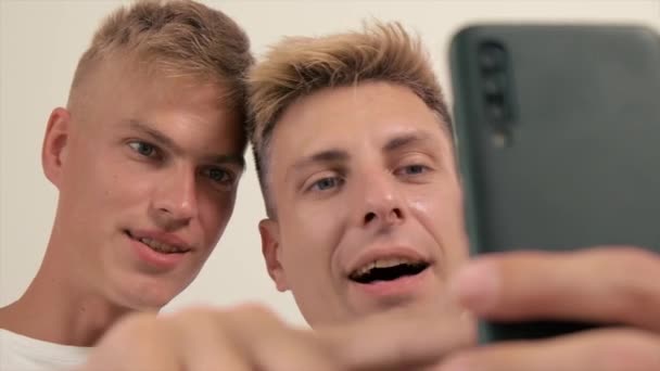 Gay casal juntos no casa no o sofá mentira mão segurando um celular. — Vídeo de Stock