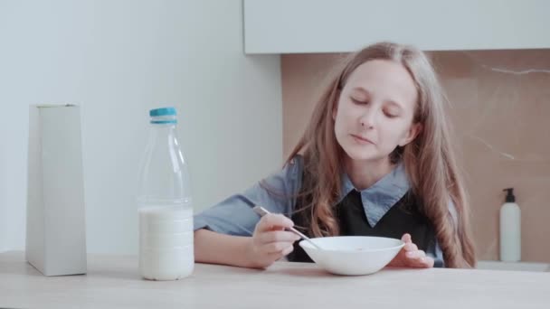 एक लड़की अनाज के साथ नाश्ता कर रही है। रसोई में खाने वाली खुश लड़की . — स्टॉक वीडियो