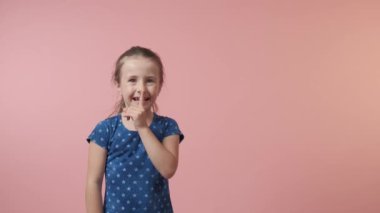 Bir kız bir tizo hareketi gösterir, dudaklarının yanında bir parmak. Puantiyeli mavi elbise.