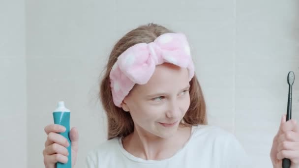 Šťastná dívka dává zubní pastu na ekologický černý kartáč, čistí si zuby. — Stock video
