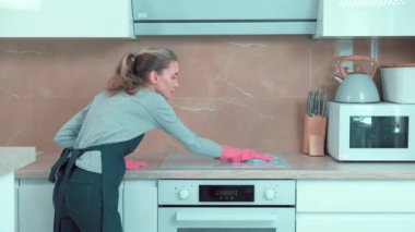 Eldivenli genç bir kadın sobanın yüzeyini yıkıyor..