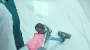 Bir kadın mutfaktaki mermer ışıklı zemini süpürüyor..