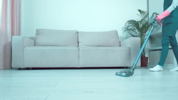 Красивая девушка пылесосит пол рядом с диваном в гостиной. — стоковое видео