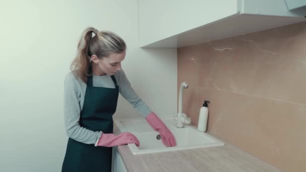 Seorang gadis cantik mencuci baskom di dapur mengenakan sarung tangan karet merah muda. — Stok Video