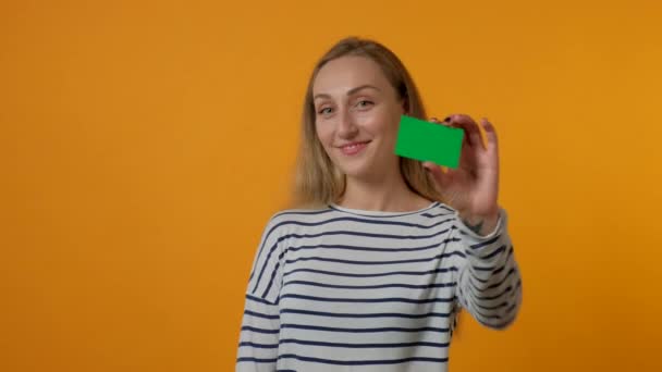 Πορτρέτο μιας νεαρής χαμογελαστής γυναίκας που κρατά μια λευκή πράσινη κάρτα στο χέρι της. 4K — Αρχείο Βίντεο