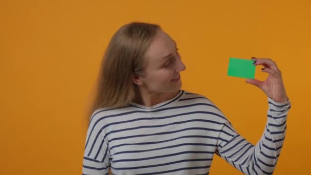 Uma bela jovem está segurando um cartão verde em branco em suas mãos e sorrindo. — Vídeo de Stock