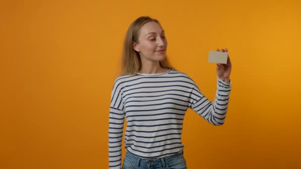 Uma jovem está mostrando um cartão cinza em branco e sorrindo. Fundo amarelo. 4K — Vídeo de Stock