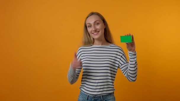 Chica feliz sosteniendo una tarjeta de plástico en su mano y mostrando un gesto hacia arriba pulgares. — Vídeos de Stock