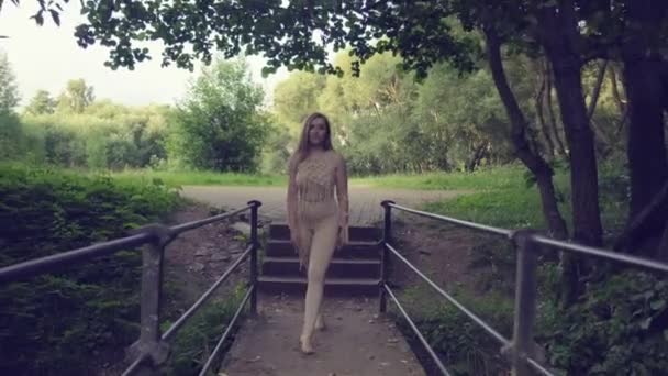 Una hermosa joven esbelta con el pelo largo y rubio está caminando por el puente. — Vídeos de Stock