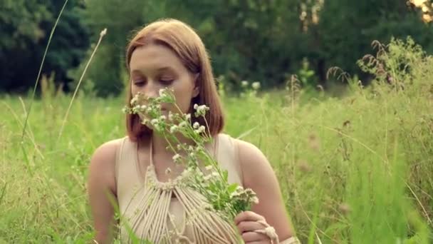 Een mooie jonge vrouw houdt een wilde bloem in haar hand en ruikt het. — Stockvideo