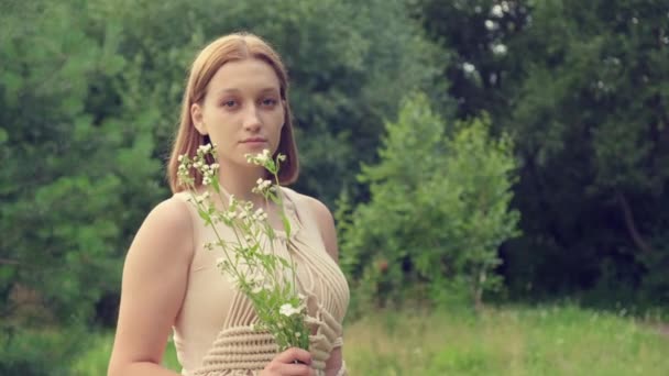 Een mooie jonge vrouw met rood haar houdt witte wilde bloemen in haar hand. — Stockvideo