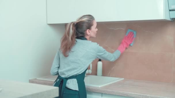 La chica limpia las baldosas de la cocina con un trapo azul, con guantes de goma. — Vídeos de Stock