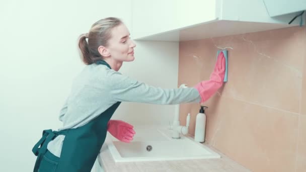 女の子はゴムピンクの手袋を着て、ラグでキッチンのタイルを拭く. — ストック動画