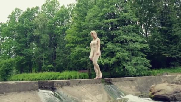 Una ragazza bionda attraversa il ponte da cui sgorga l'acqua. Bellezza naturale. — Video Stock