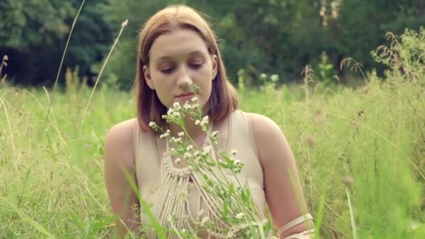 Una hermosa joven con el pelo rojo sostiene una flor salvaje en su mano. — Vídeo de stock