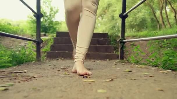 Piernas de una chica delgada en leggings camina hacia adelante a través del puente. — Vídeo de stock