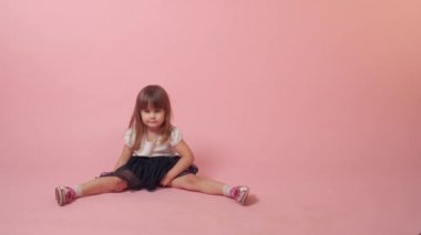 Küçük kız yerde oturuyor, gülümsüyor ve kameraya bakıyor..