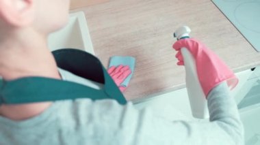 Bir temizlikçi kız mutfaktaki bir dolaba temizleyici sprey sıkar..