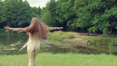 Uzun saçlı sarışın bir kız gölün ve ormanın arka planında dönüyor..