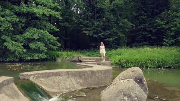 Una hermosa joven camina a lo largo de un puente de hormigón, el agua en ambos lados. — Vídeo de stock