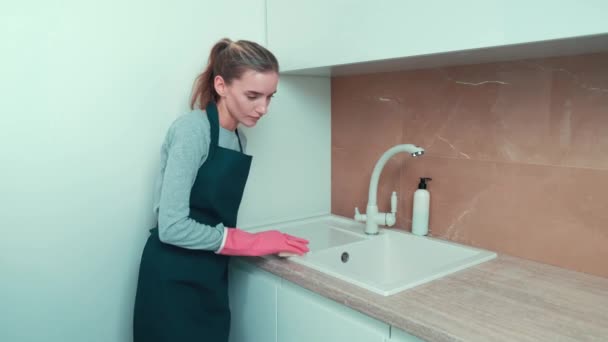 Gadis muda dalam sarung tangan merah muda mencuci keran dengan spons dengan agen pembersih. — Stok Video