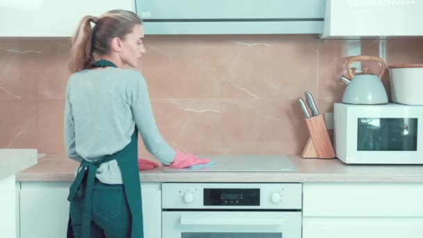 Een vrouw in handschoenen wast het oppervlak van de keuken fornuis met een doek, wasmiddel. — Stockvideo
