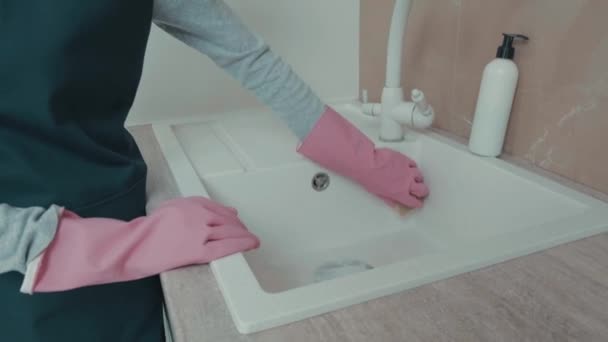 Seorang gadis muda mencuci wastafel di dapur mengenakan sarung tangan merah muda. Pembersihan rumah — Stok Video