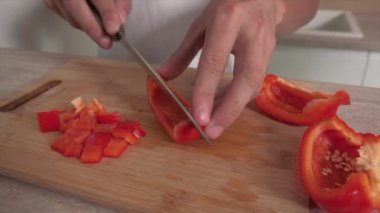Tişörtlü bir adam salata yapmak için kırmızı biberi keskin bir bıçakla keser..