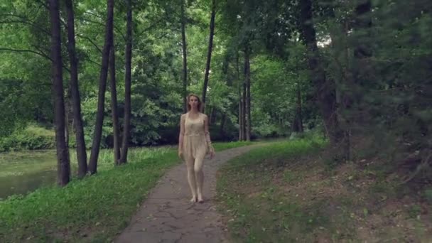 Młoda piękna szczupła dziewczyna spaceruje wzdłuż drogi z lasu. — Wideo stockowe