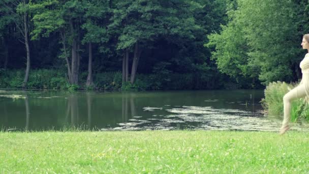 Красивая грациозная девушка танцует на фоне озера и леса. — стоковое видео