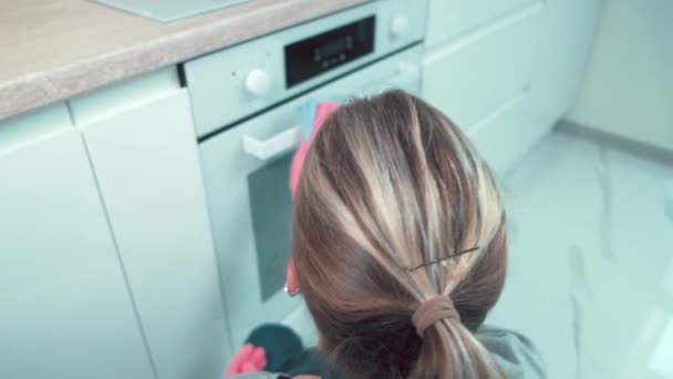 Una mano con un guanto di gomma pulisce la maniglia della porta del forno. Vista dal retro. — Video Stock