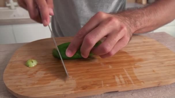 De man snijdt een komkommer met een scherp mes voor het maken van salade. — Stockvideo