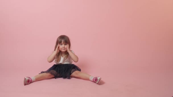 Милая маленькая девочка сидит на полу и балуется, улыбается гримасы. — стоковое видео