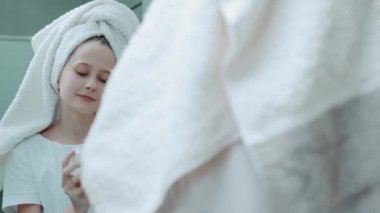 Kafasında havlu olan güzel bir kız yüzüne nemlendirici sürüyor..