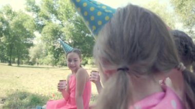 Kızlar doğum günlerinin şerefine kadeh tokuştururlar. Parkta parti.