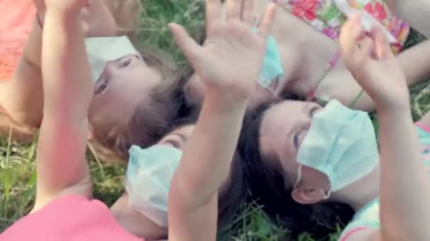 Skupina dívek leží na trávě v parku v lékařských maskách. — Stock video