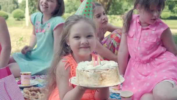 La chica mira a la cámara y sostiene un pastel en sus manos. Niños felices. — Vídeo de stock