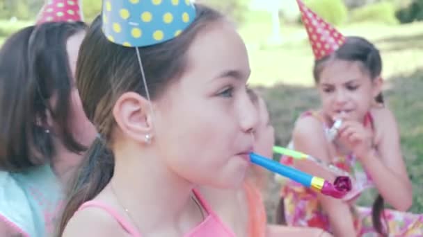 Χαρούμενη ομάδα παιδιών γιορτάζουν τα γενέθλιά τους στον κήπο με σφυρίχτρα. — Αρχείο Βίντεο