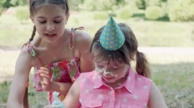 Kızın yüzünde krem şanti var, kirli bir yüz. Doğum günü kutlamaları.