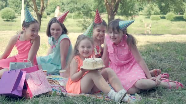 Las chicas se sientan en el césped del parque. Está sosteniendo un pastel de cumpleaños en sus manos. — Vídeo de stock