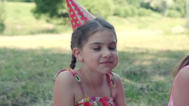 Una chica con gorra festiva se está comiendo un pastel. Celebrando un cumpleaños en el parque. — Vídeo de stock
