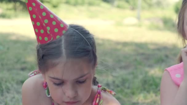 お祝いの帽子の女の子は彼女の誕生日を祝い、ケーキを食べる. — ストック動画