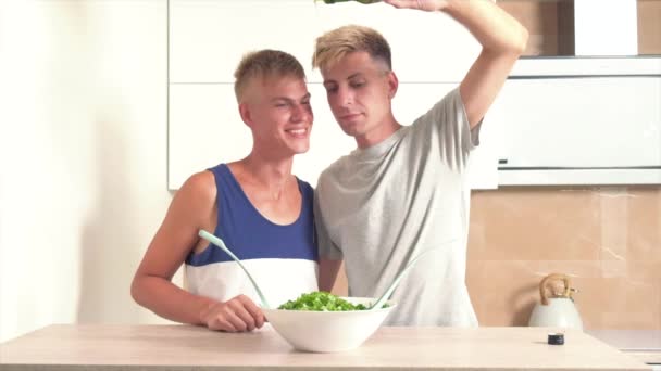 Huile qui est versée dans la salade. Deux amateurs de gars cuisinent ensemble et s'embrassent. — Video