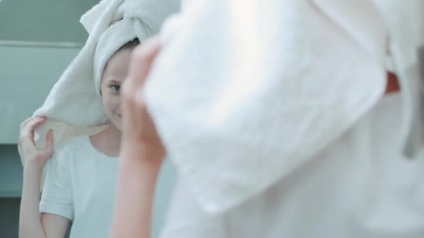 En vacker flicka med en handduk på huvudet ser sig i spegeln. Morgonrutin. — Stockvideo